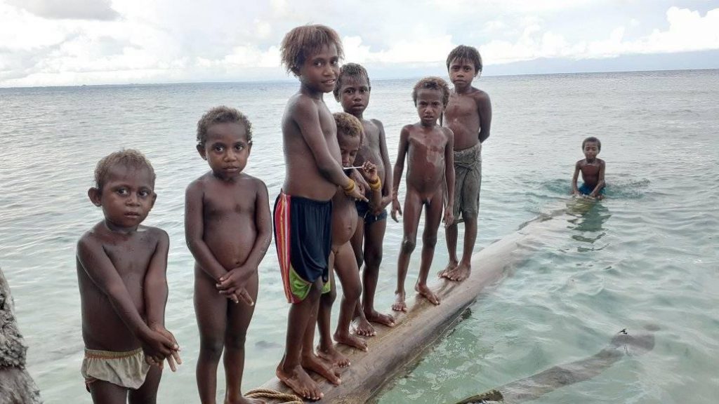 A dozen children floating on a log in the bay