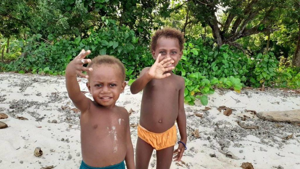 Two children on the beach waving at you